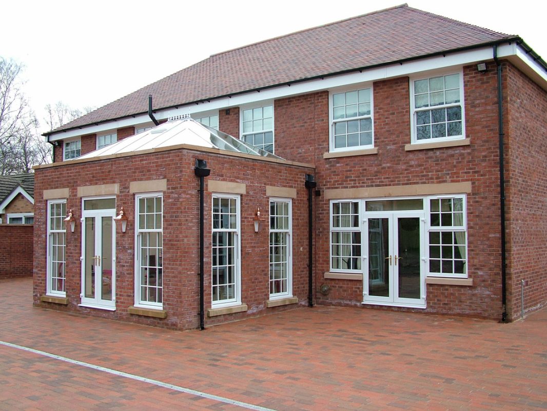 tall white uPVC Georgian style sash windows on a red brick home and orangery extension.