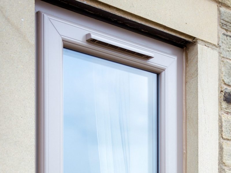Close-up of a trickle vent fitted into a uPVC window frame, providing background ventilation for improved airflow