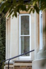 White narrow uPVC sash window set against a cream-coloured house wall