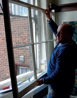 man holding sash window pane to window opening