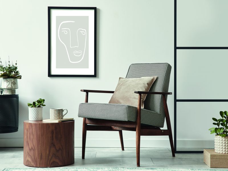 Scandinavian-style living room featuring a design armchair, black poster frame, wooden stool, and modern decor