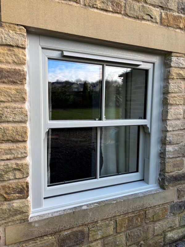 Close-up of white uPVC sliding sash window with trickle vent in stone wall, showing modern efficiency.