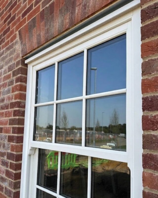 White uPVC sash window with concealed head vent and astragal bars on a stone property